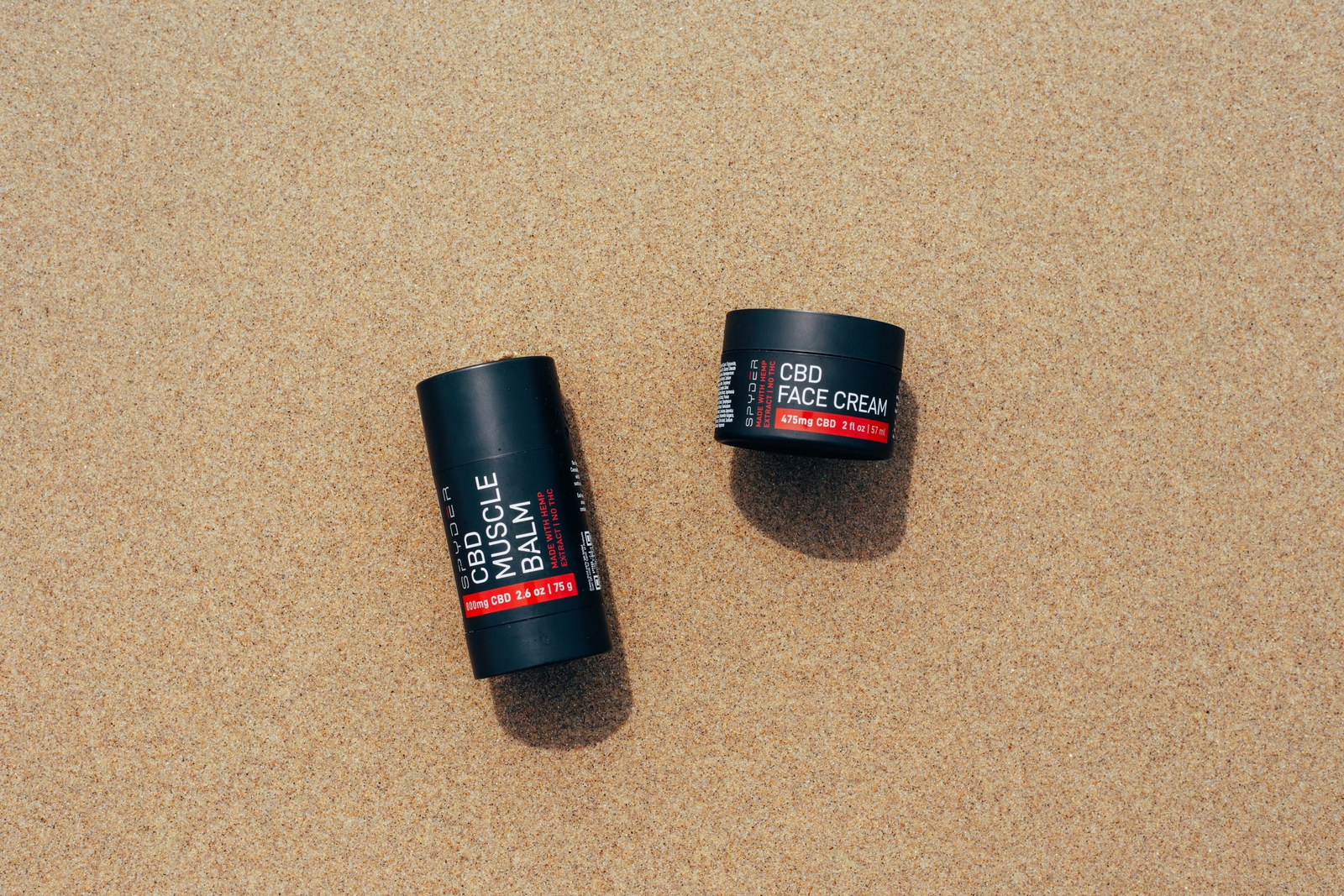 Spyder CBD muscle balm and face cream laid on clean sand