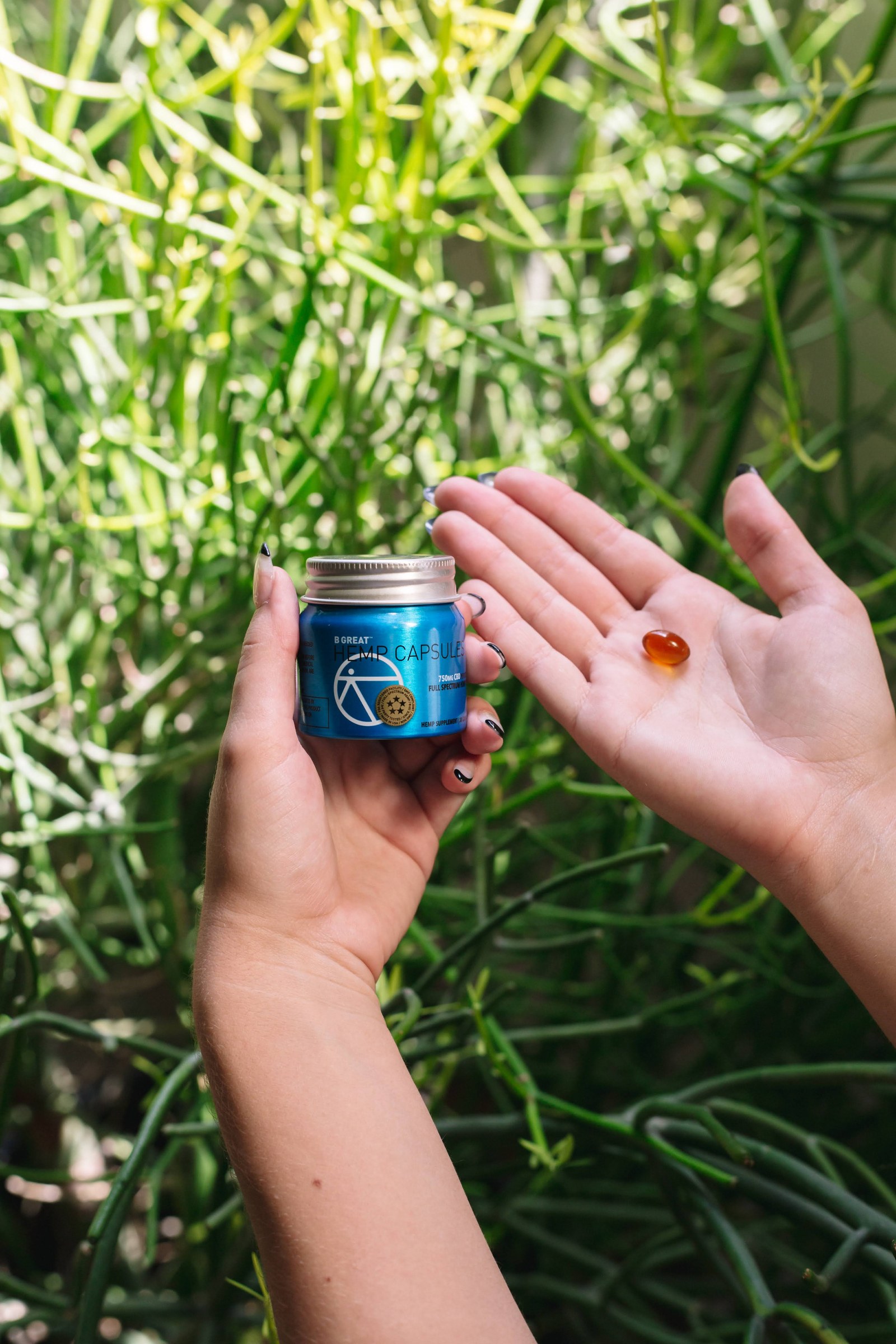 A single amber softgel resting in an open palm beside the jar