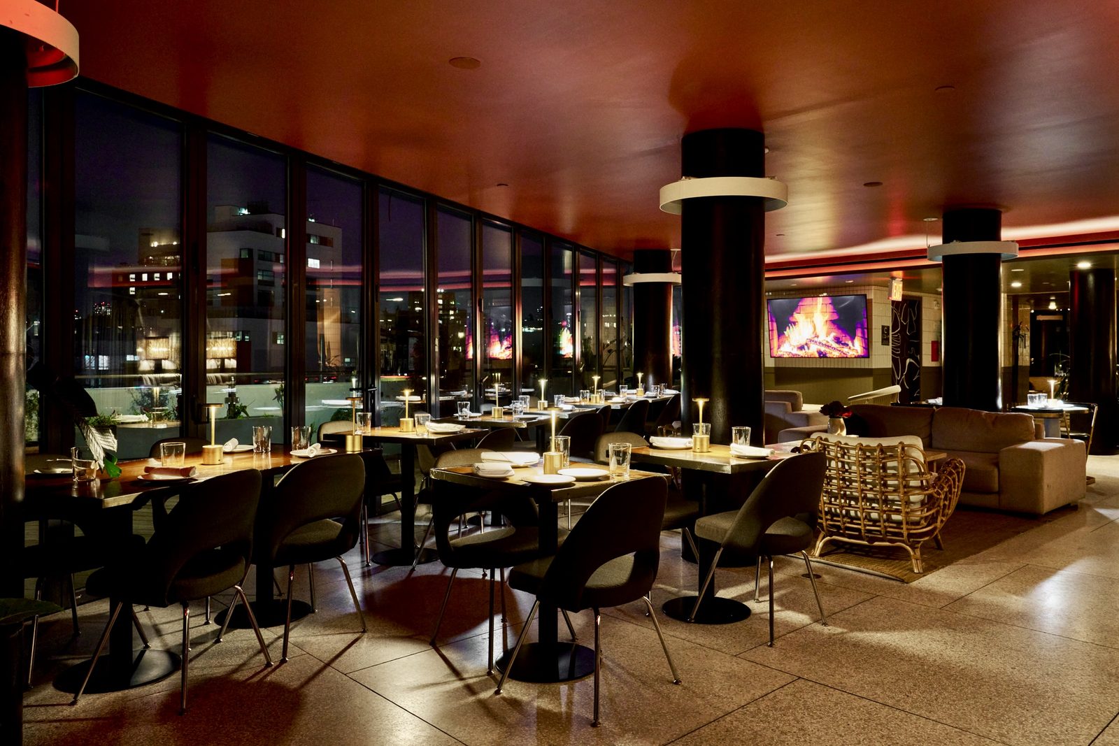 Hotel Indigo dining room at night, fireplace lit and tables set along the windows