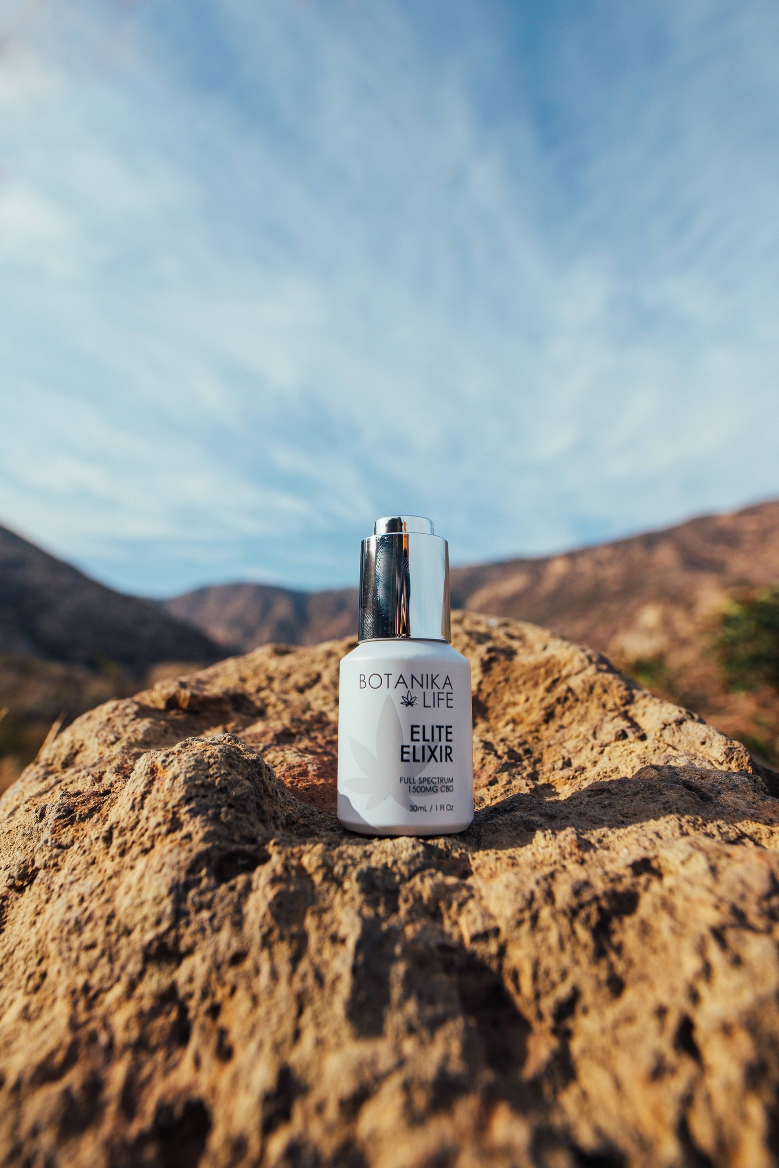 Botanika Life Elite Elixir bottle standing on a boulder with mountains behind