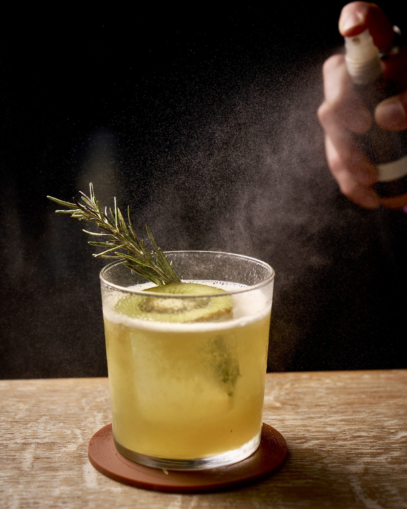 Bartender spraying an aromatic finish over a cocktail garnished with rosemary