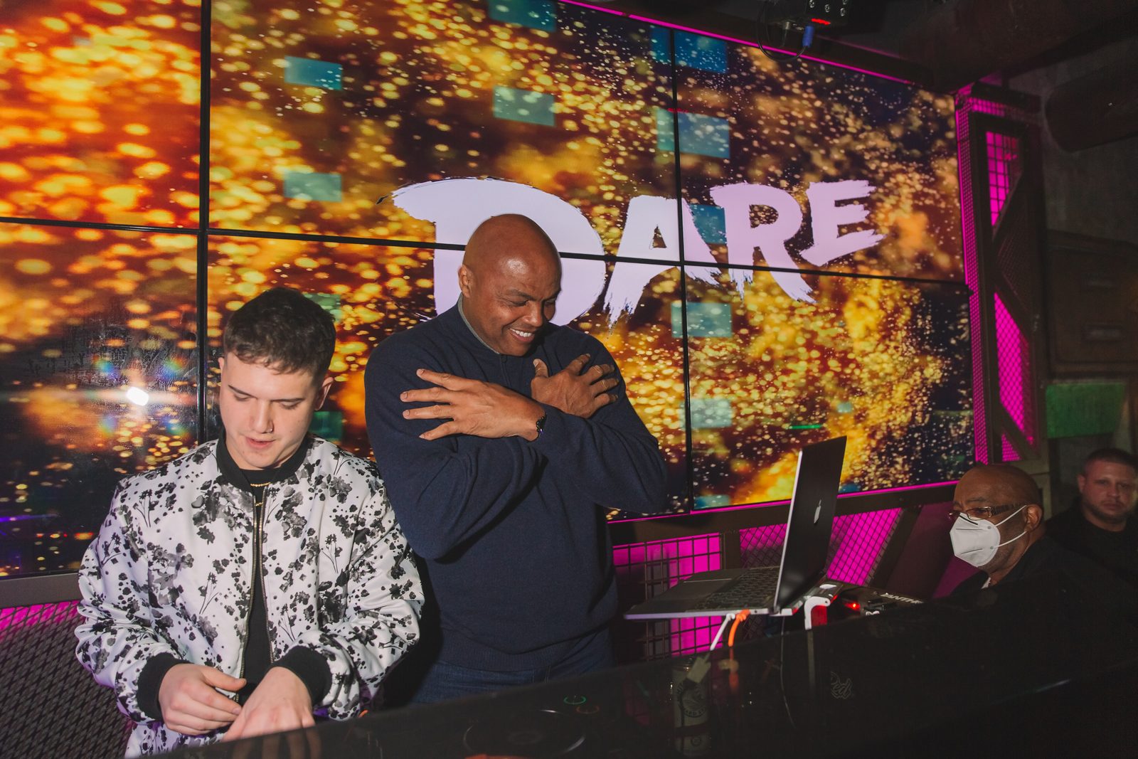 Charles Barkley beside the DJ booth lit by the screen wall