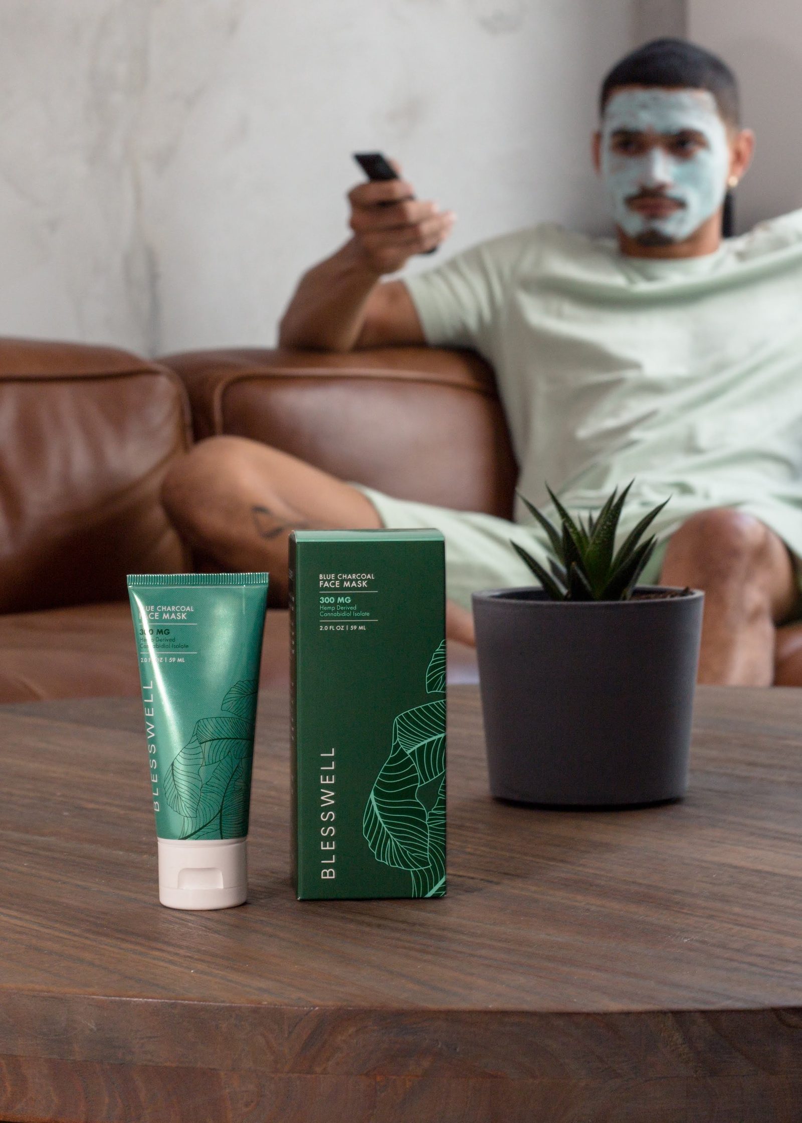 Man in a clay mask on the sofa with BLESSWELL product on the table