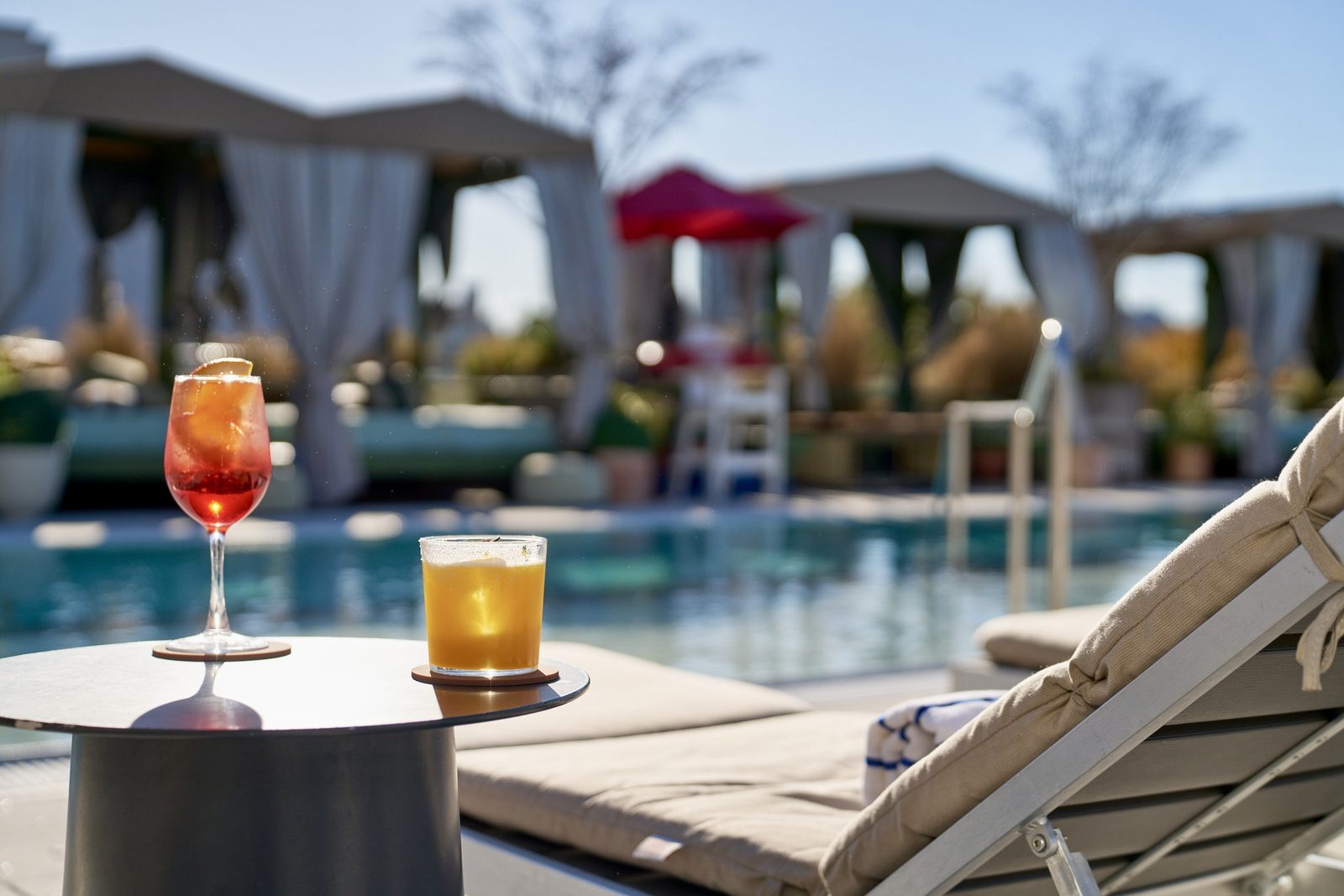 Drinks set on a table beside the rooftop pool at Hotel Indigo, cabanas and loungers behind