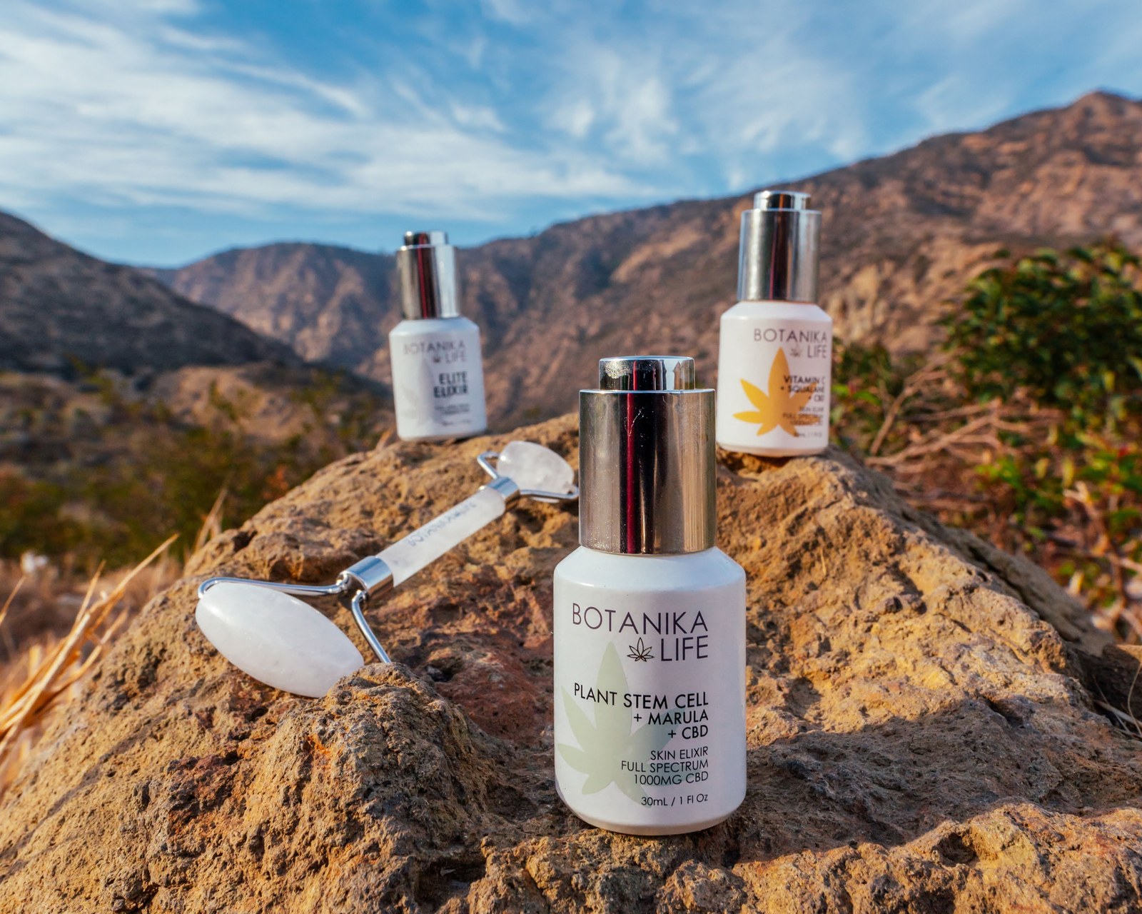 Botanika Life serum, crystal face roller and second bottle grouped on a boulder