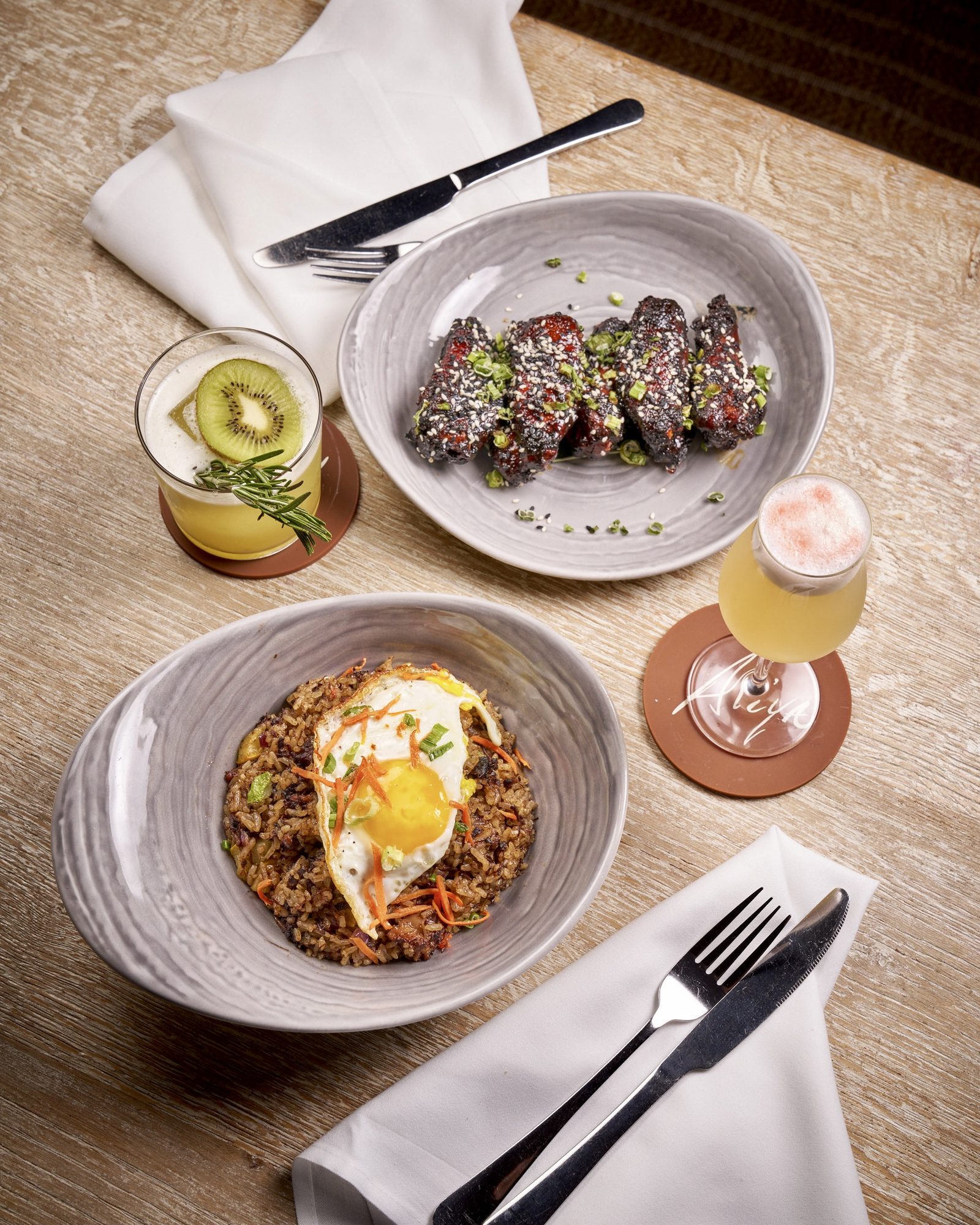 Two plated dishes with cocktails and cutlery on a linen-set table, shot from above